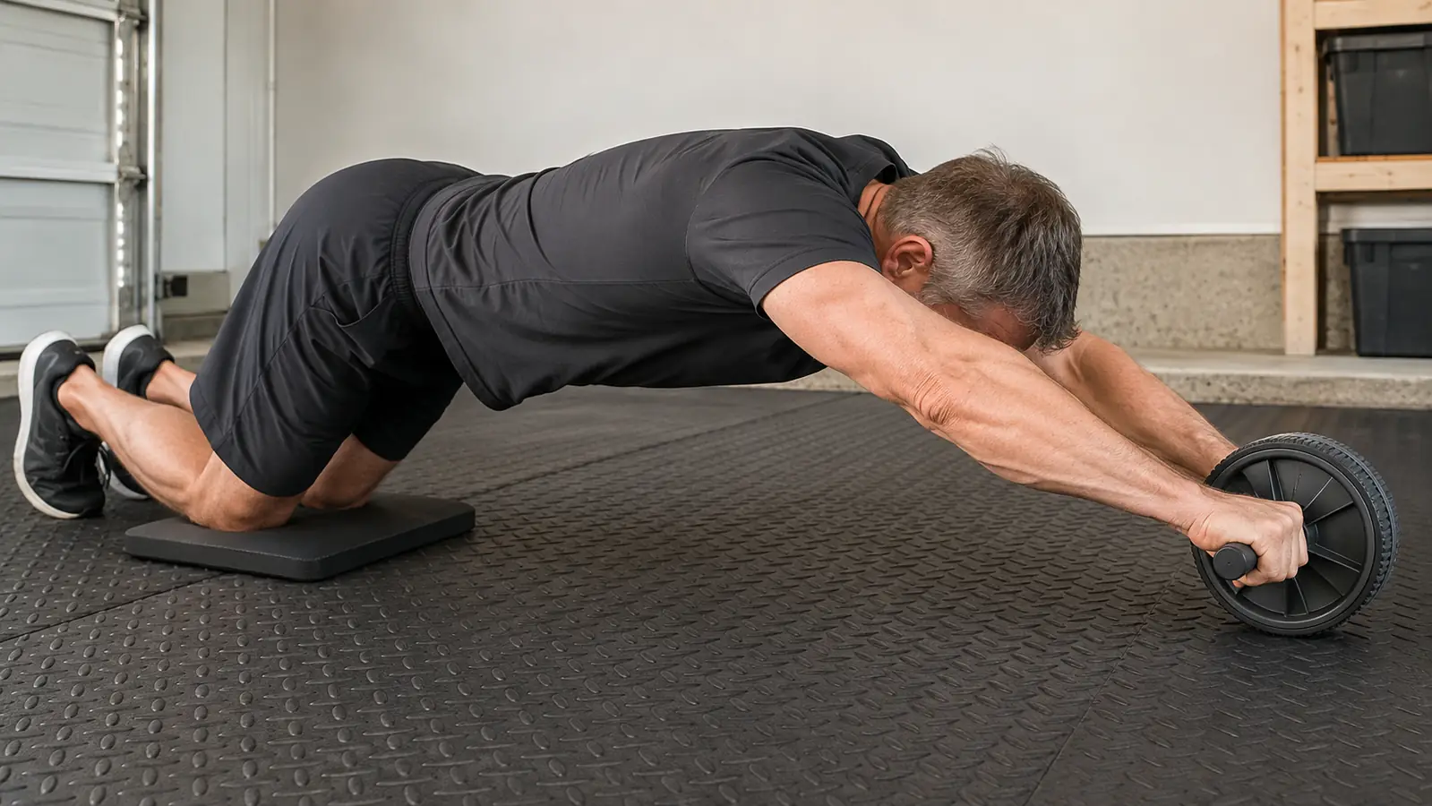 Knees on the padded knee mat, hands gripping the ab roller handles, rolling forward across a rubber garage mat.