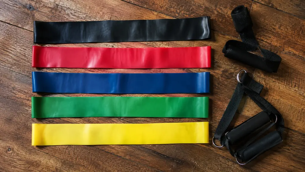 Two resistance band sets laid out side by side on a wood floor, five bands laid straight with a pair of handles and a door anchor beside them.